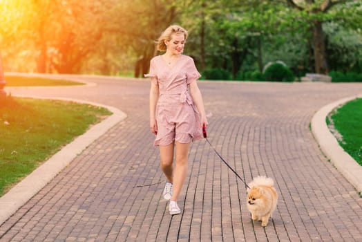 Attractive young woman holding dog spitz outside and smiling at camera, walking in the park. Concept about friendship between people and animals.