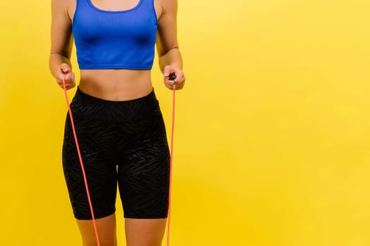 Fit female athlete with jumping with rope during fitness training against yellow background