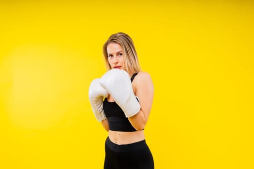 Woman boxer in gloves training on a yellow and dark studio background