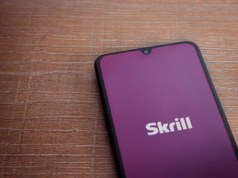 Lod, Israel - July 16,2023: Skrill app launch screen on smartphone on wooden background. Top view flat lay with copy space.