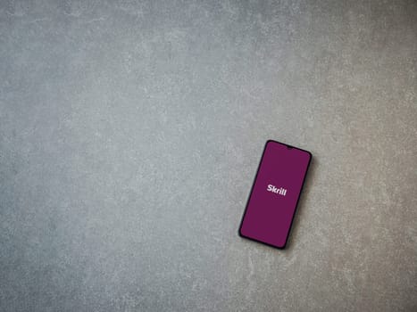 Lod, Israel - July 16,2023: Skrill app launch screen on smartphone on ceramic stone background. Top view flat lay with copy space.