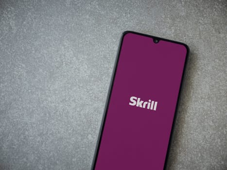 Lod, Israel - July 16,2023: Skrill app launch screen on smartphone on ceramic stone background. Top view flat lay with copy space.
