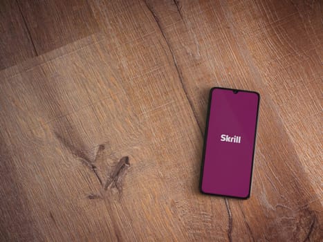 Lod, Israel - July 16,2023: Skrill app launch screen on smartphone on wooden background. Top view flat lay with copy space.