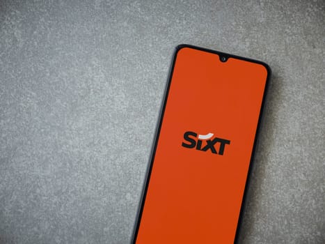 Lod, Israel - July 16,2023: SIXT rent app launch screen on smartphone on ceramic stone background. Top view flat lay with copy space.