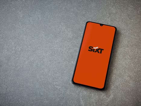 Lod, Israel - July 16,2023: SIXT rent app launch screen on smartphone on ceramic stone background. Top view flat lay with copy space.