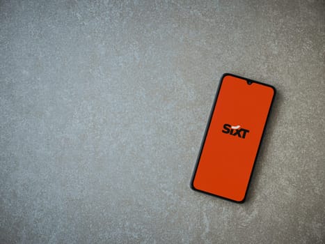 Lod, Israel - July 16,2023: SIXT rent app launch screen on smartphone on ceramic stone background. Top view flat lay with copy space.