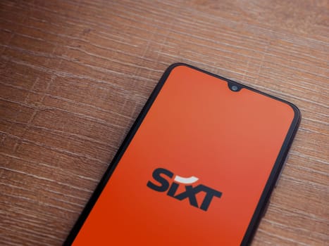 Lod, Israel - July 16,2023: SIXT rent app launch screen on smartphone on wooden background. Top view flat lay with copy space.
