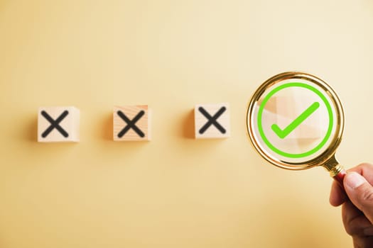 Hand holding a magnifying glass focuses on the right choice concept, with a checkmark or tick symbol next to wrong cross icons. Emphasizing the importance of making the correct decision.