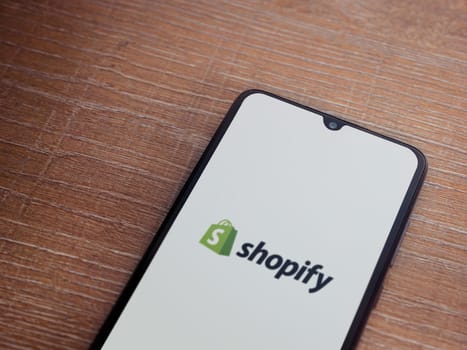 Lod, Israel - July 16,2023: Shopify app launch screen on smartphone on wooden background. Top view flat lay with copy space.