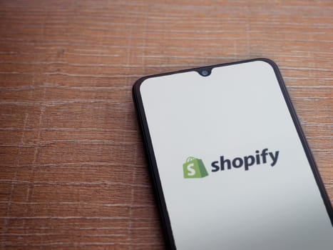 Lod, Israel - July 16,2023: Shopify app launch screen on smartphone on wooden background. Top view flat lay with copy space.