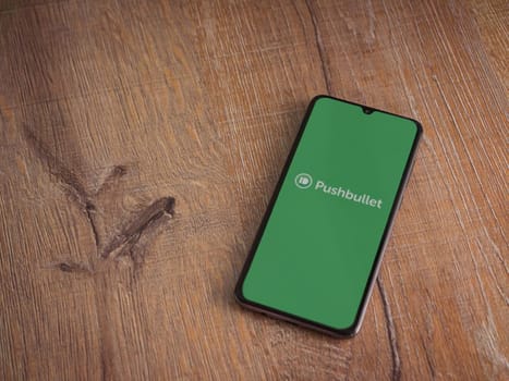 Lod, Israel - July 16,2023: Pushbullet app launch screen on smartphone on wooden background. Top view flat lay with copy space.