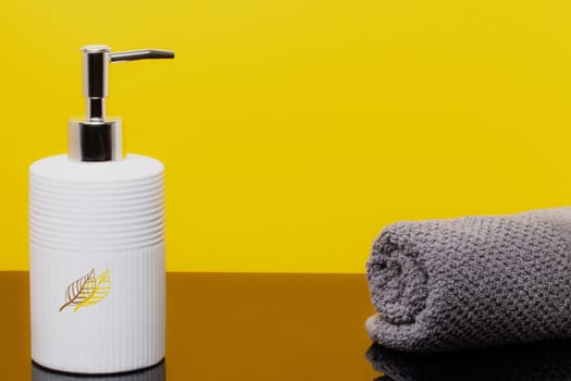 Macro of a beauty cosmetic makeup bottle and a fresh soft terry bath towel on brown table over yellow background. Copy space for product display montage.
