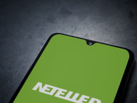 Lod, Israel - July 16,2023: NETELLER app launch screen on smartphone on dark marble stone background. Top view flat lay with copy space.