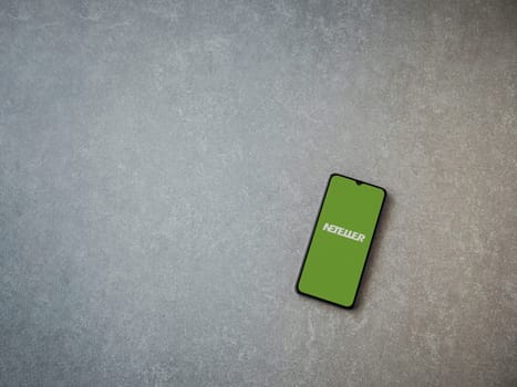 Lod, Israel - July 16,2023: NETELLER app launch screen on smartphone on ceramic stone background. Top view flat lay with copy space.