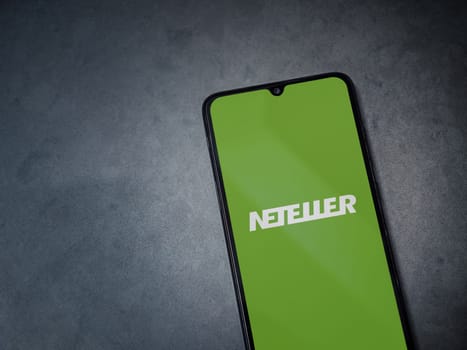 Lod, Israel - July 16,2023: NETELLER app launch screen on smartphone on dark marble stone background. Top view flat lay with copy space.