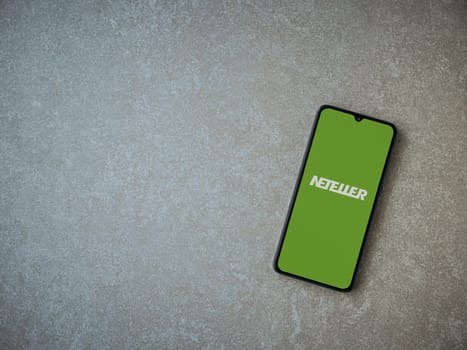 Lod, Israel - July 16,2023: NETELLER app launch screen on smartphone on ceramic stone background. Top view flat lay with copy space.