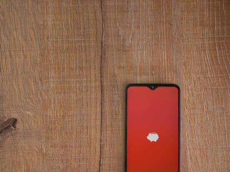 Lod, Israel - July 16,2023: Money Manager Expense & Budget app launch screen on smartphone on wooden background. Top view flat lay with copy space.