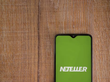 Lod, Israel - July 16,2023: NETELLER app launch screen on smartphone on wooden background. Top view flat lay with copy space.