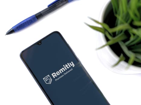 Lod, Israel - July 16,2023: Modern workspace with smartphone with Remitly app launch screen on white background. Close up top view flat lay.