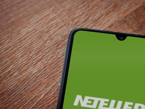 Lod, Israel - July 16,2023: NETELLER app launch screen on smartphone on wooden background. Top view flat lay with copy space.