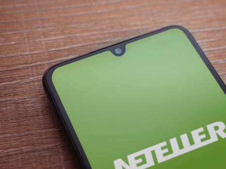 Lod, Israel - July 16,2023: NETELLER app launch screen on smartphone on wooden background. Top view flat lay with copy space.