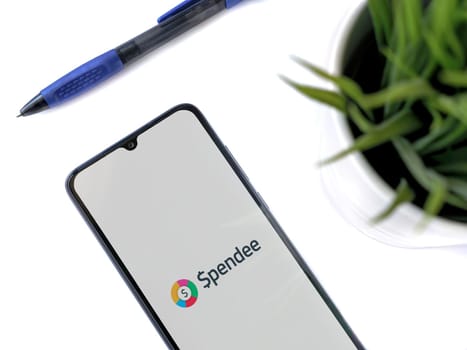 Lod, Israel - July 16,2023: Modern workspace with smartphone with Spendee app launch screen on white background. Close up top view flat lay.