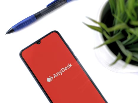 Lod, Israel - July 16,2023: Modern workspace with smartphone with Anydesk app launch screen on white background. Close up top view flat lay.