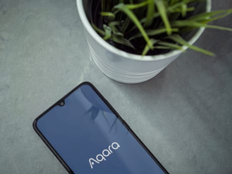 Lod, Israel - July 16,2023: Modern workspace with smartphone with Aqara Home app launch screen on marble background. Close up top view flat lay.