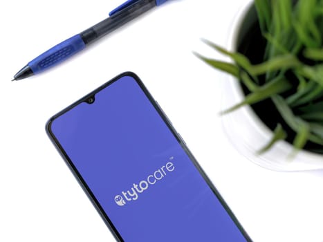 Lod, Israel - July 16,2023: Modern workspace with smartphone with TytoCare app launch screen on white background. Close up top view flat lay.