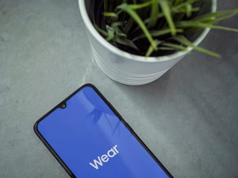 Lod, Israel - July 16,2023: Modern workspace with smartphone with Wear - Galaxy Wearable app launch screen on marble background. Close up top view flat lay.