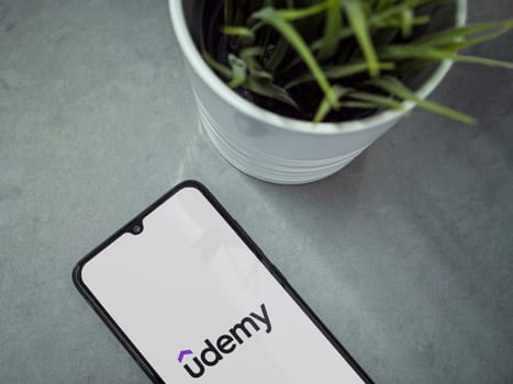 Lod, Israel - July 16,2023: Modern workspace with smartphone with Udemy app launch screen on marble background. Close up top view flat lay.