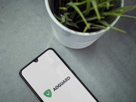 Lod, Israel - July 16,2023: Modern workspace with smartphone with AdGuard app launch screen on marble background. Close up top view flat lay.