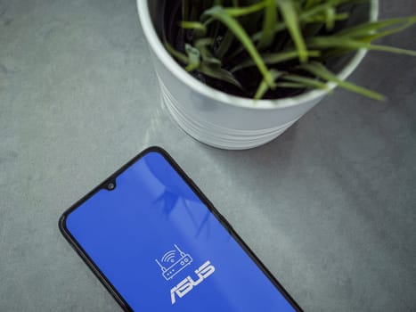 Lod, Israel - July 16,2023: Modern workspace with smartphone with ASUS Router app launch screen on marble background. Close up top view flat lay.