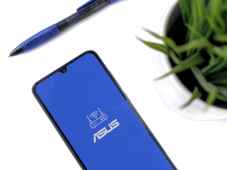 Lod, Israel - July 16,2023: Modern workspace with smartphone with ASUS Router app launch screen on white background. Close up top view flat lay.