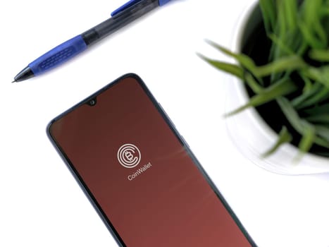 Lod, Israel - July 16,2023: Modern workspace with smartphone with CoinWallet app launch screen on white background. Close up top view flat lay.