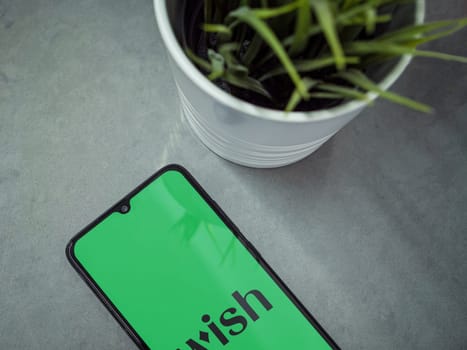 Lod, Israel - July 16,2023: Modern workspace with smartphone with Wish app launch screen on marble background. Close up top view flat lay.