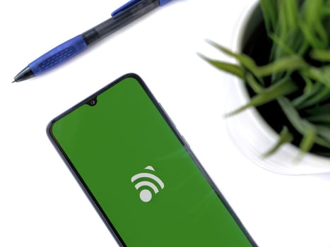 Lod, Israel - July 16,2023: Modern workspace with smartphone with Unified Remote app launch screen on white background. Close up top view flat lay.