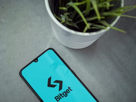 Lod, Israel - July 16,2023: Modern workspace with smartphone with Bitget app launch screen on marble background. Close up top view flat lay.