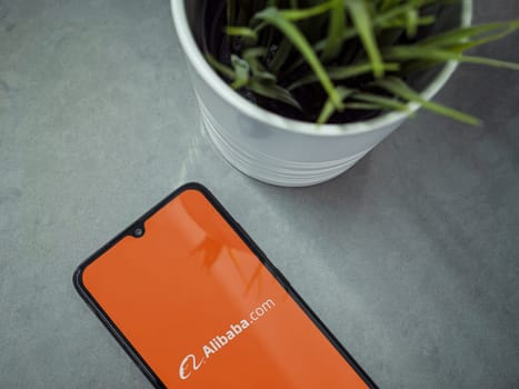 Lod, Israel - July 16,2023: Modern workspace with smartphone with Alibaba.com app launch screen on marble background. Close up top view flat lay.