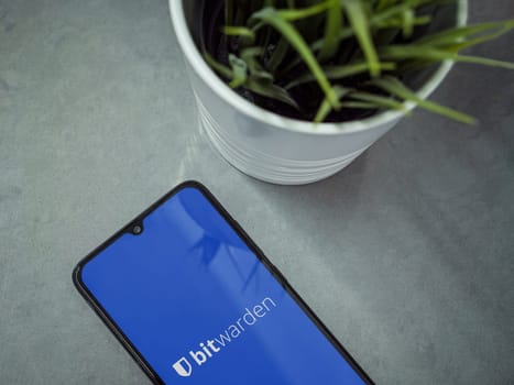 Lod, Israel - July 16,2023: Modern workspace with smartphone with Bitwarden Password Manager app launch screen on marble background. Close up top view flat lay.