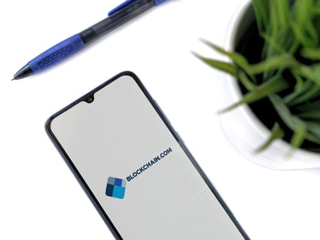 Lod, Israel - July 16,2023: Modern workspace with smartphone with Blockchain.com app launch screen on white background. Close up top view flat lay.