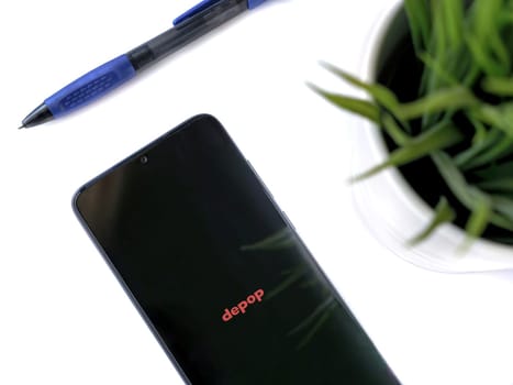 Lod, Israel - July 16,2023: Modern workspace with smartphone with Depop app launch screen on white background. Close up top view flat lay.