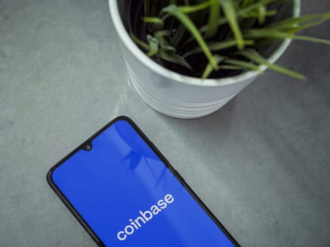 Lod, Israel - July 16,2023: Modern workspace with smartphone with Coinbase app launch screen on marble background. Close up top view flat lay.