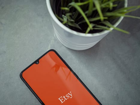 Lod, Israel - July 16,2023: Modern workspace with smartphone with Etsy app launch screen on marble background. Close up top view flat lay.