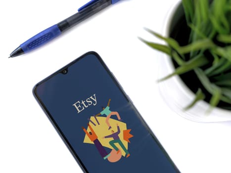 Lod, Israel - July 16,2023: Modern workspace with smartphone with Etsy Seller app launch screen on white background. Close up top view flat lay.