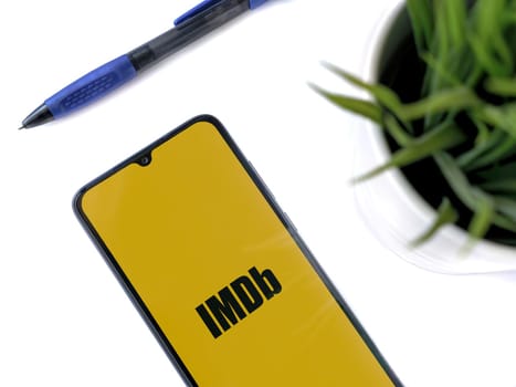 Lod, Israel - July 16,2023: Modern workspace with smartphone with IDMb app launch screen on white background. Close up top view flat lay.