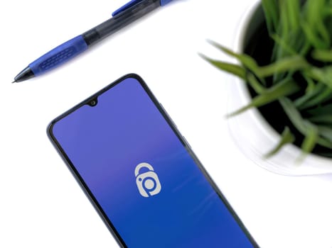 Lod, Israel - July 16,2023: Modern workspace with smartphone with IDrive Photo Backup app launch screen on white background. Close up top view flat lay.
