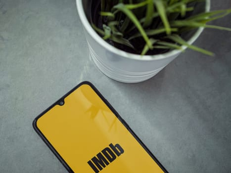 Lod, Israel - July 16,2023: Modern workspace with smartphone with IDMb app launch screen on marble background. Close up top view flat lay.