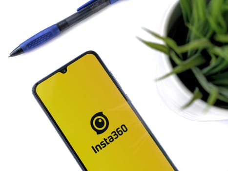 Lod, Israel - July 16,2023: Modern workspace with smartphone with Insta360 app launch screen on white background. Close up top view flat lay.