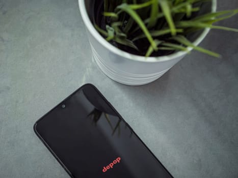 Lod, Israel - July 16,2023: Modern workspace with smartphone with Depop app launch screen on marble background. Close up top view flat lay.